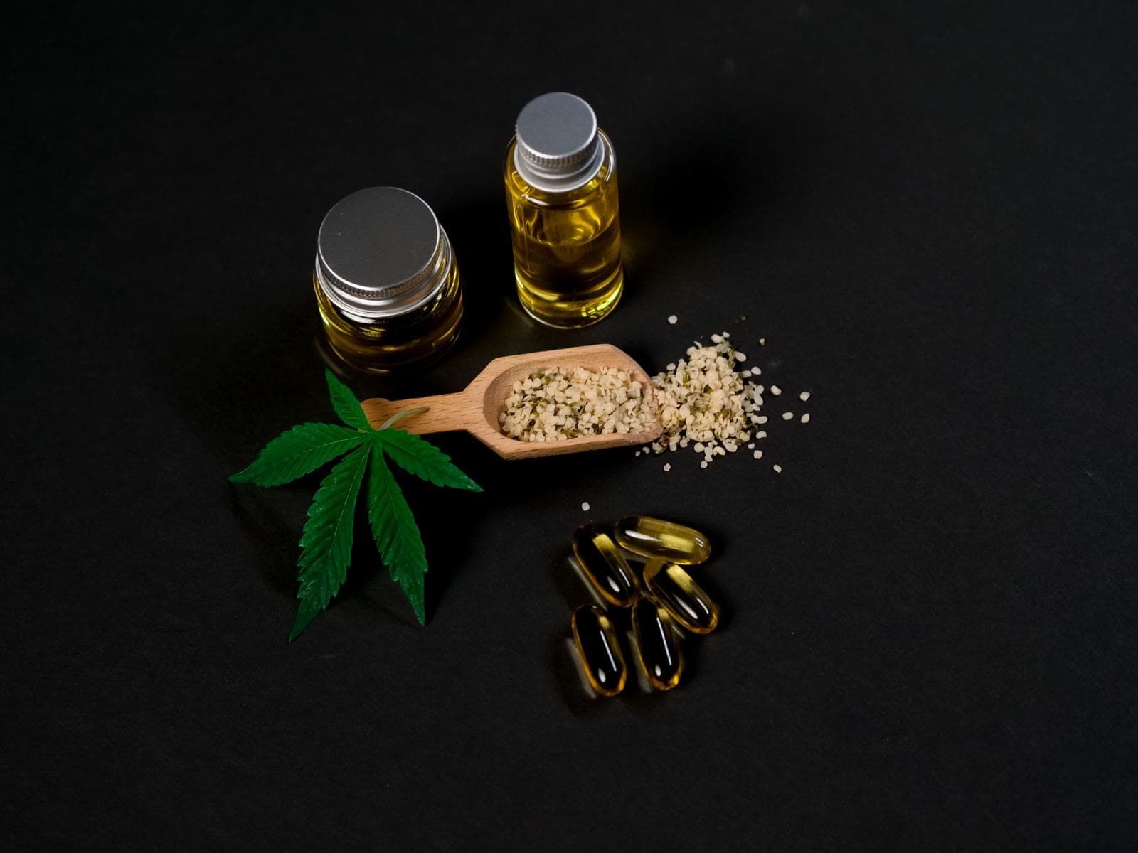 Hemp oil, capsules, and seeds arranged with a cannabis leaf on a dark surface